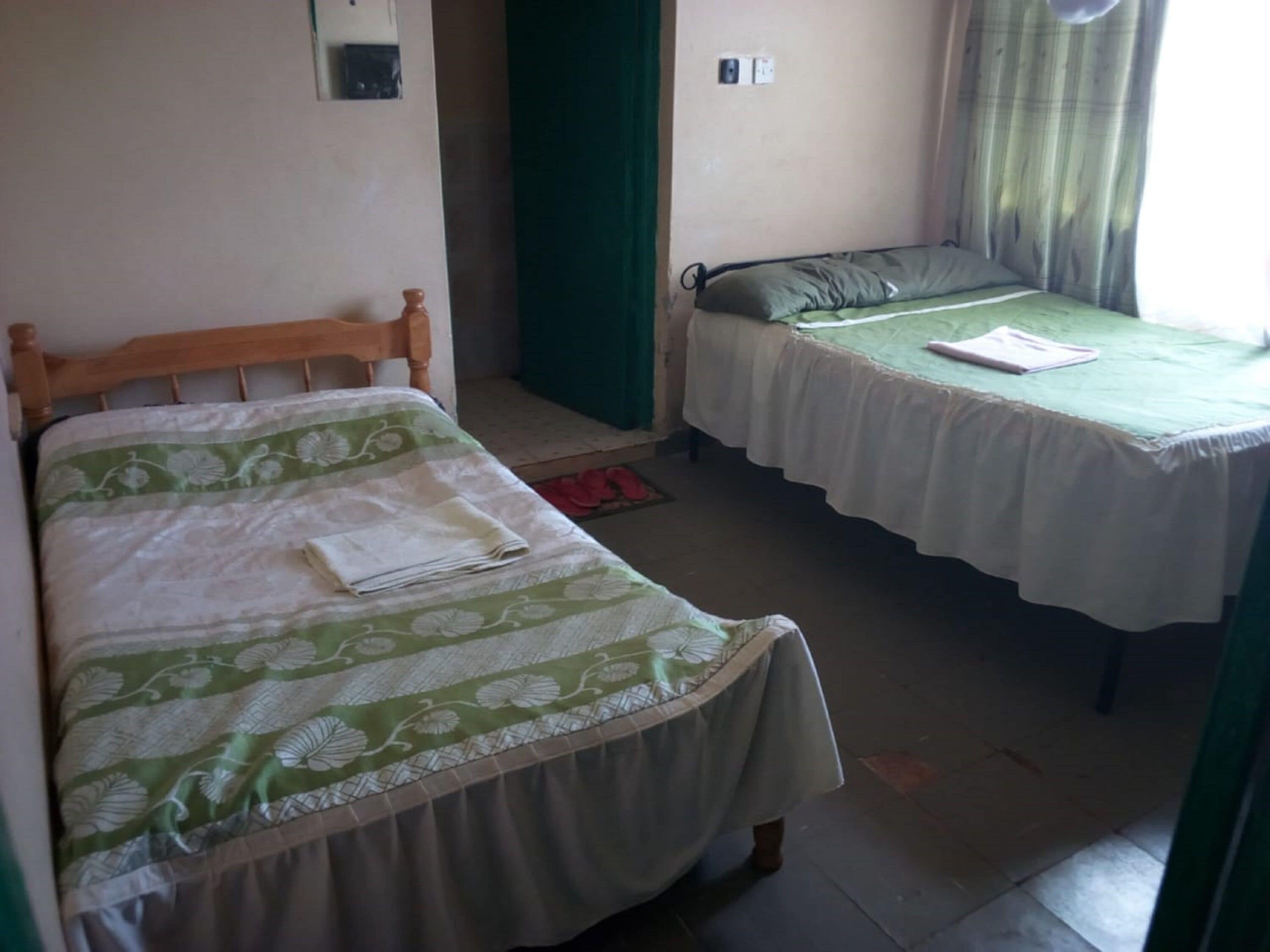 A room with two beds, each with a green and white floral bedspread.