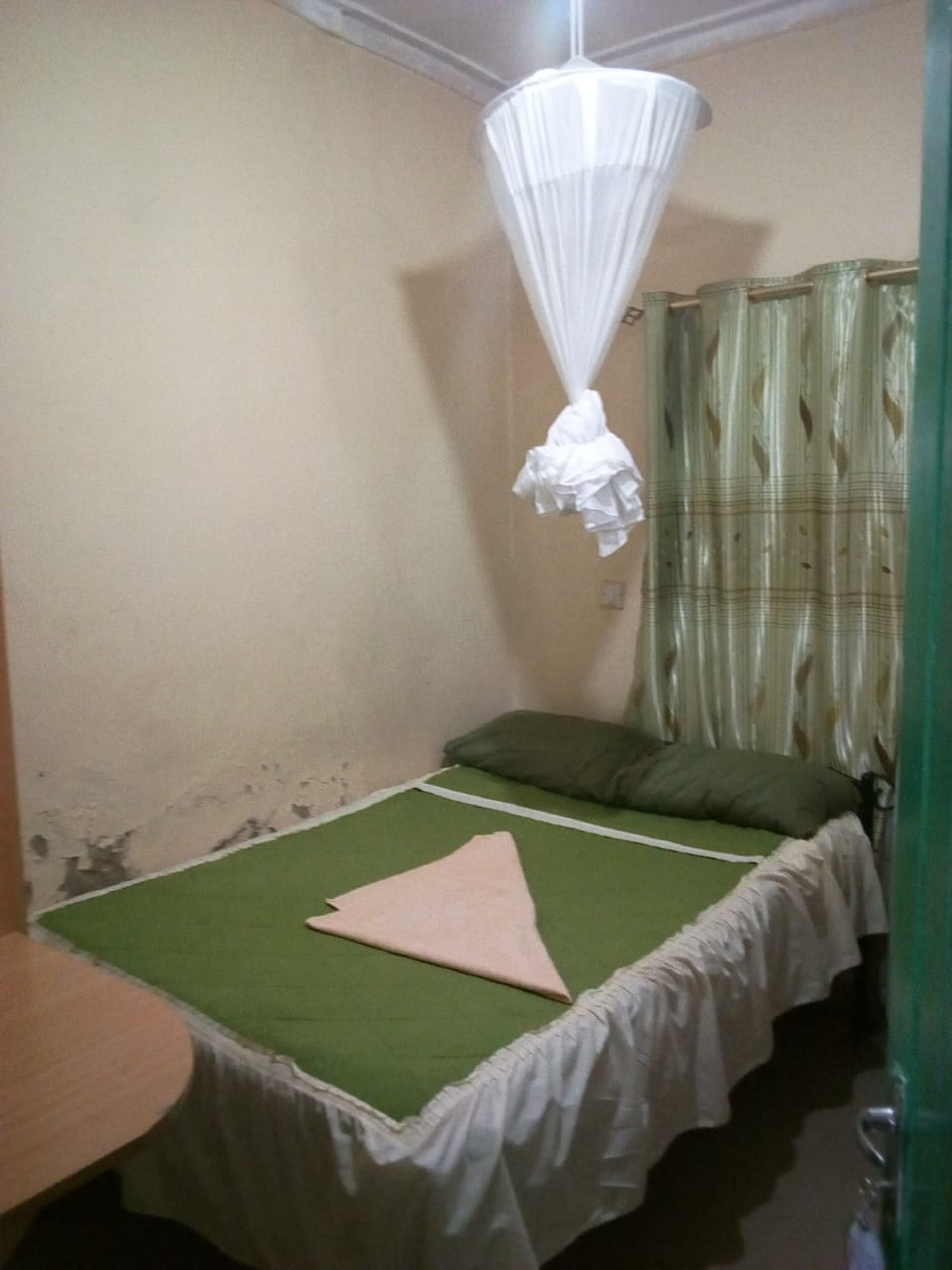 Una habitación pequeña y sencilla con una cama individual, una mosquitera y una cortina.