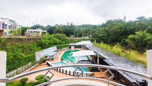 A rooftop pool area with multiple pools and a covered seating area, surrounded by lush greenery and buildings in the background. - OYO 2065 Holly Sentosa Hotel (Batam)