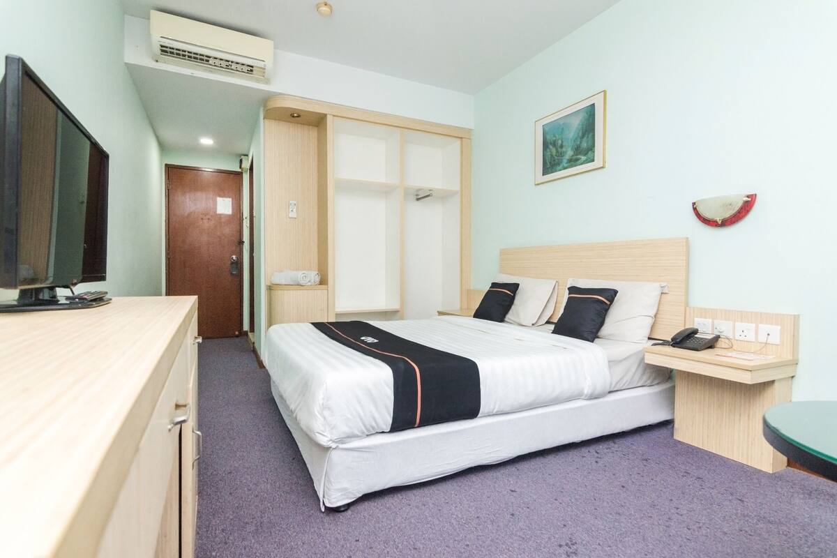 A hotel room with a bed, bedside table, TV, wardrobe, and a painting on the wall.