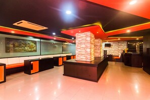 Um lobby moderno com balcão de recepção, área de estar e uma parede decorativa em pedra.