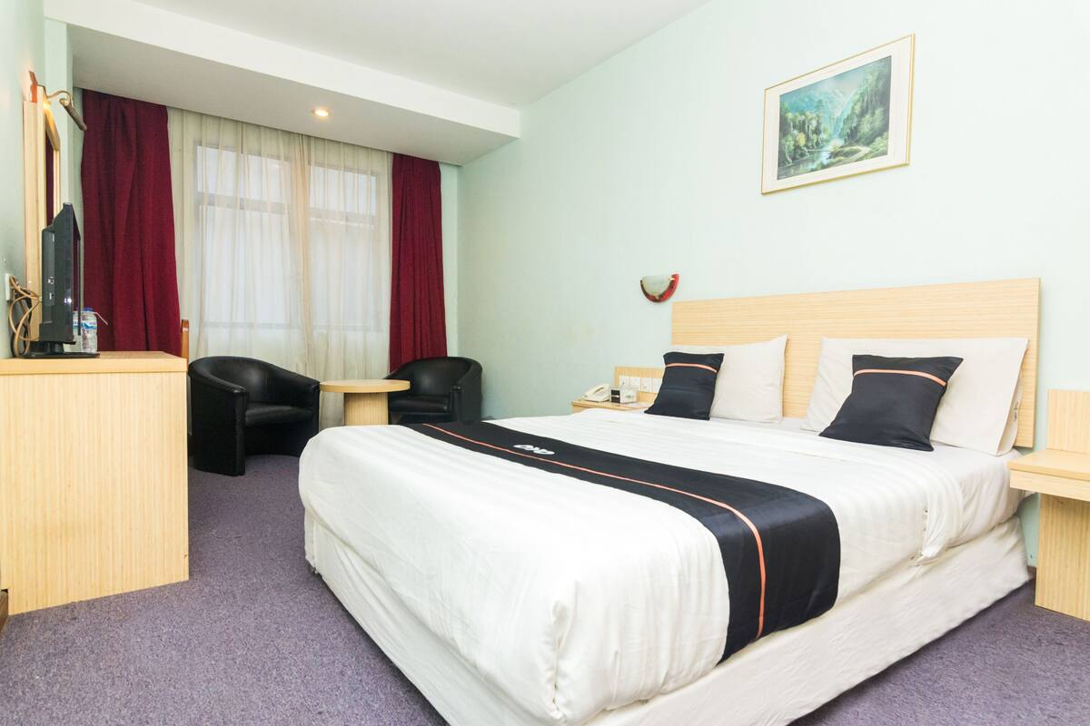 A hotel room with a large bed, a desk with a chair, a small table, and a painting on the wall.