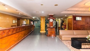 A hotel lobby with a reception desk, a clock, a sofa, and a staircase in the background. - OYO 2065 Holly Sentosa Hotel (Batam)