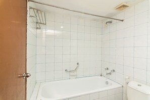 Bathroom features a bathtub, toilet, and shower area with a grid-patterned tile wall and a handrail above the bathtub.