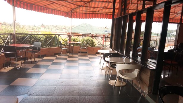 An outdoor café with checkered flooring, metal chairs, and tables under a striped awning. - Embu Prime Hotel (Embu)