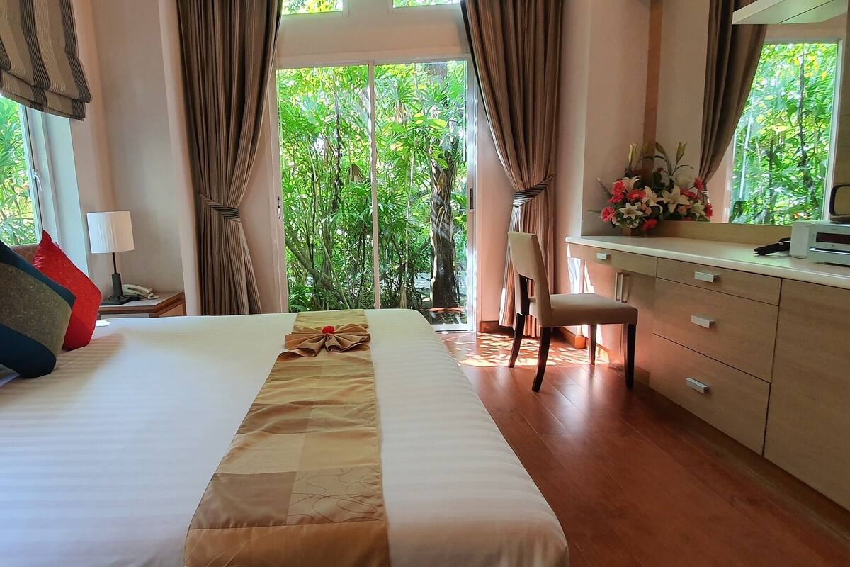 Habitación de hotel con cama, escritorio, silla y vistas a zonas verdes.