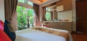 A bedroom with a bed, a desk, and a view of greenery through large windows. - T Resort Palai (Chalong)