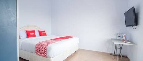 A neatly made bed with a white and red bedspread, a small bedside table with a bottle and a box, and a wall-mounted TV.