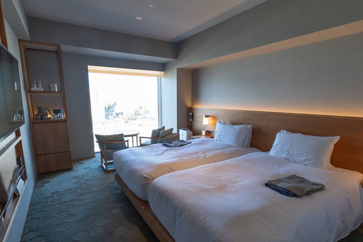 A hotel room with two large beds, a wooden wardrobe, a small table, and a chair.
