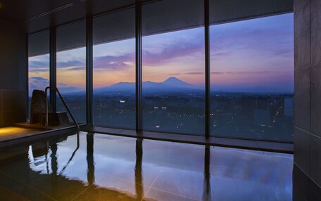 A modern indoor swimming pool with large windows offering a cityscape view at dusk.
