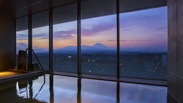 A modern indoor swimming pool with large windows offering a cityscape view at dusk. - Fujisan Mishima Tokyu Hotel (Mishima)