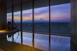 A modern indoor swimming pool with large windows offering a cityscape view at dusk.
