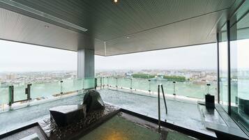 Un intérieur moderne avec une grande baie vitrée donnant sur un paysage urbain et une étendue d’eau.