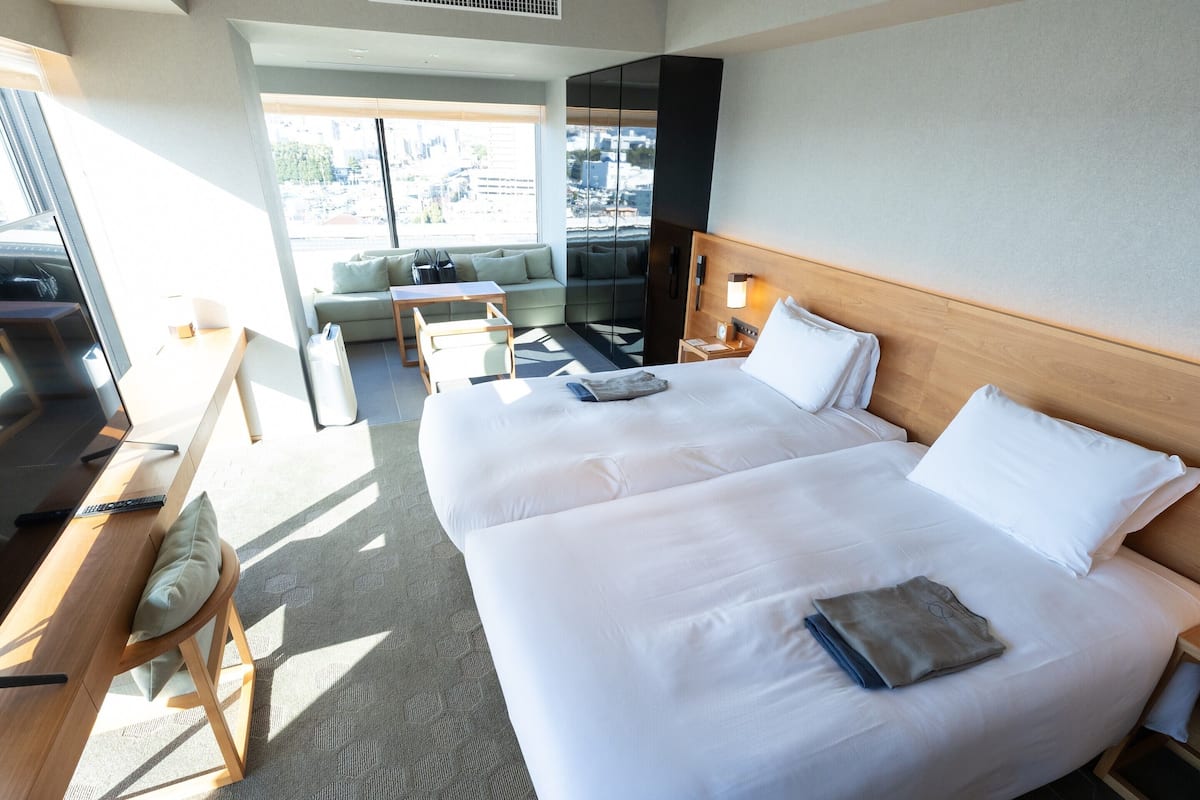 A hotel room with two beds, a desk, a chair, a small table, and a sofa.