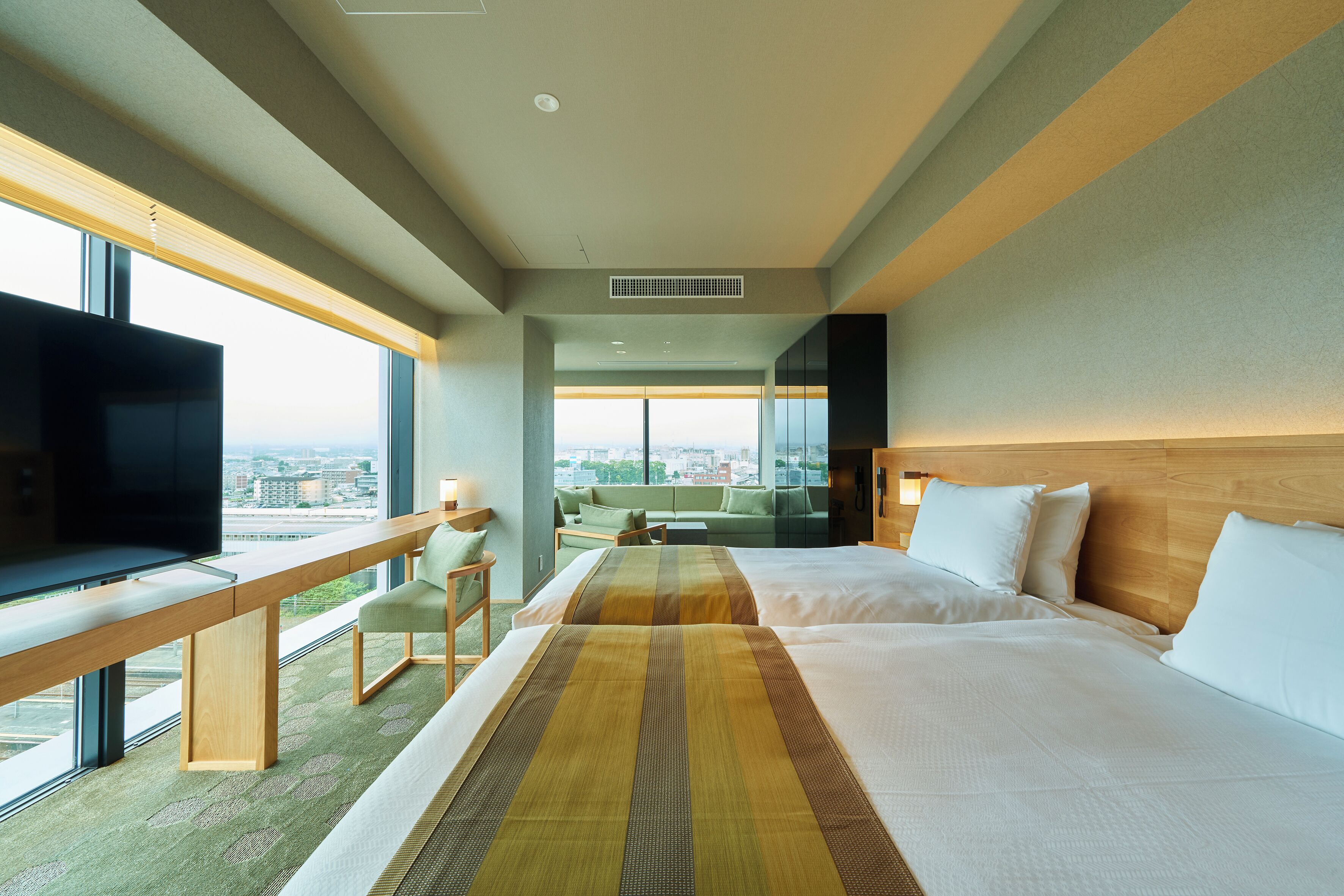 A hotel room with a large bed, a desk with a TV, a view of the city, and a balcony.