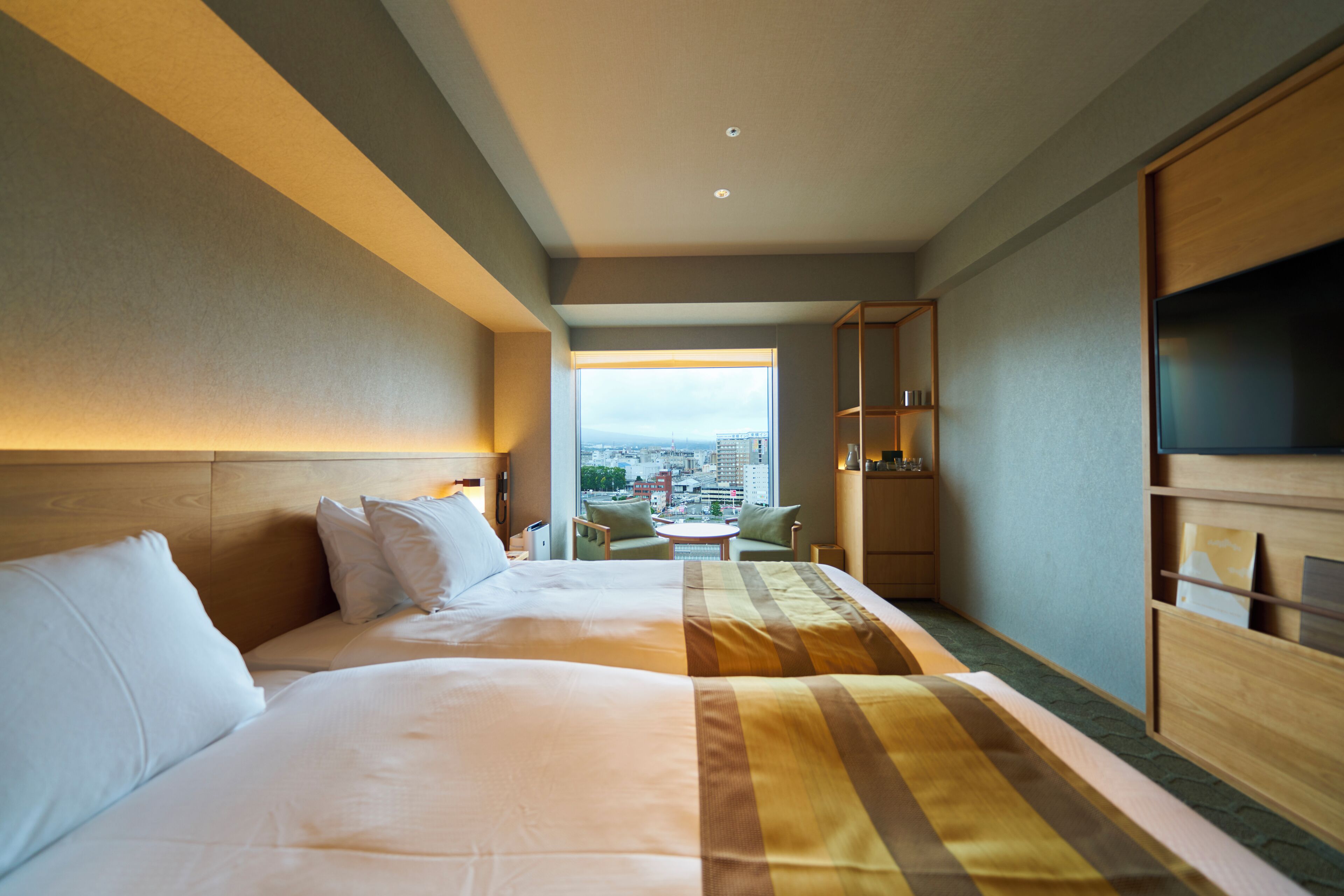 A hotel room with two beds, a view of the city, and a small table with chairs.