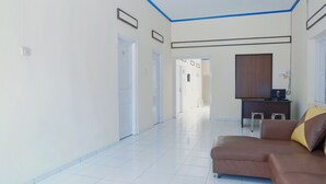 A hotel room with a large window, a brown sofa, a desk with a computer, and a mirror on the wall. - OYO 1190 Griya Soeratin Residence Syariah (Pacitan)