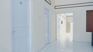 A hallway with white doors, a tiled floor, and a wooden panel on the right wall. - OYO 1190 Griya Soeratin Residence Syariah (Pacitan)