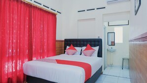 A hotel room with a bed, red curtains, a black headboard, and a white wall. - OYO 1190 Griya Soeratin Residence Syariah (Pacitan)