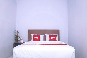 Ein Hotelzimmer mit einem Bett, zwei Kissen mit dem Schriftzug "OYO", einem Nachttisch mit einer Wasserflasche, einer Taschentuchbox und einer Vase mit Blumen.