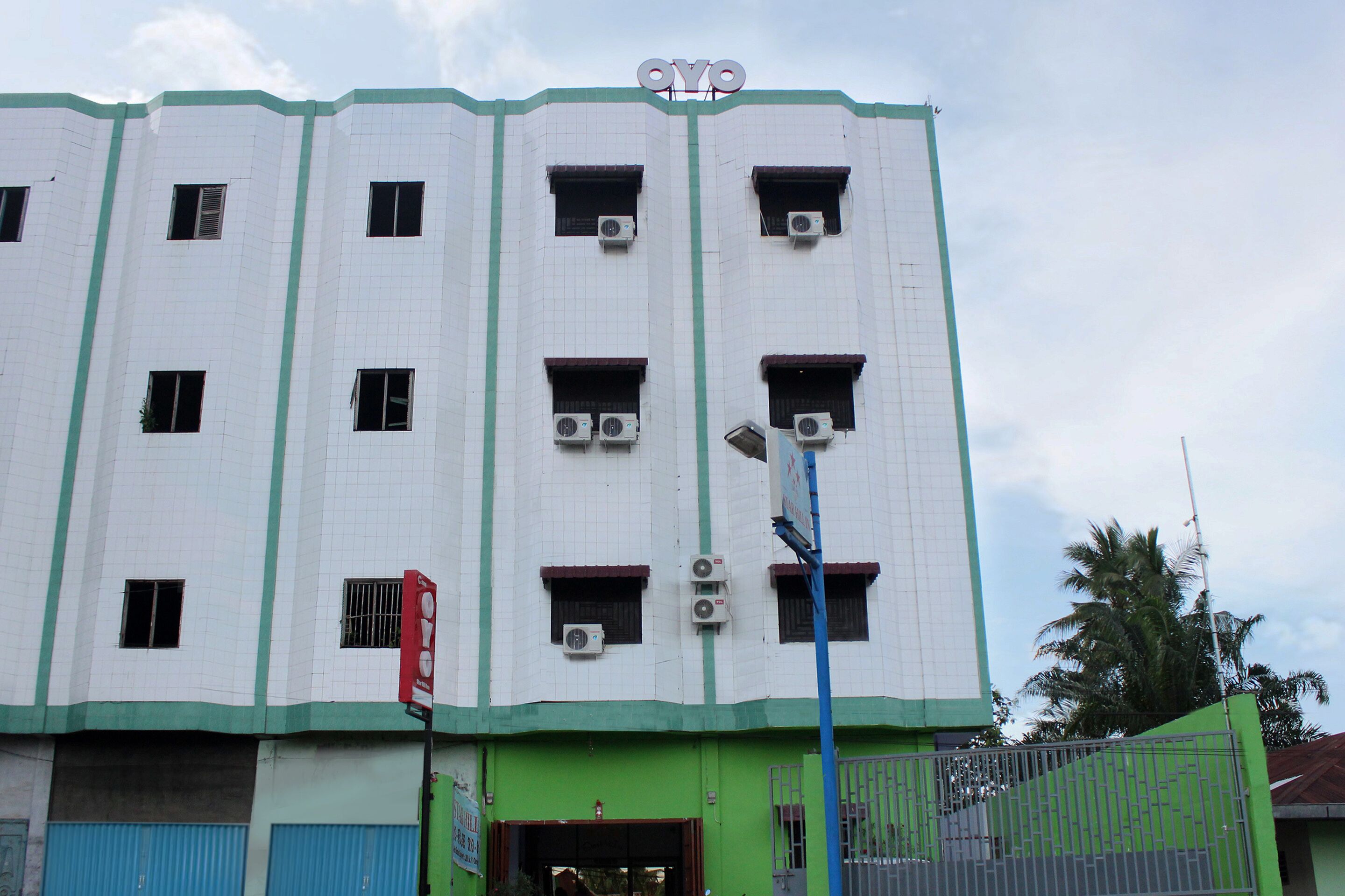 A multi-story building with a green and white facade, multiple air conditioning units, and a sign with the letters "OYO" at the top.