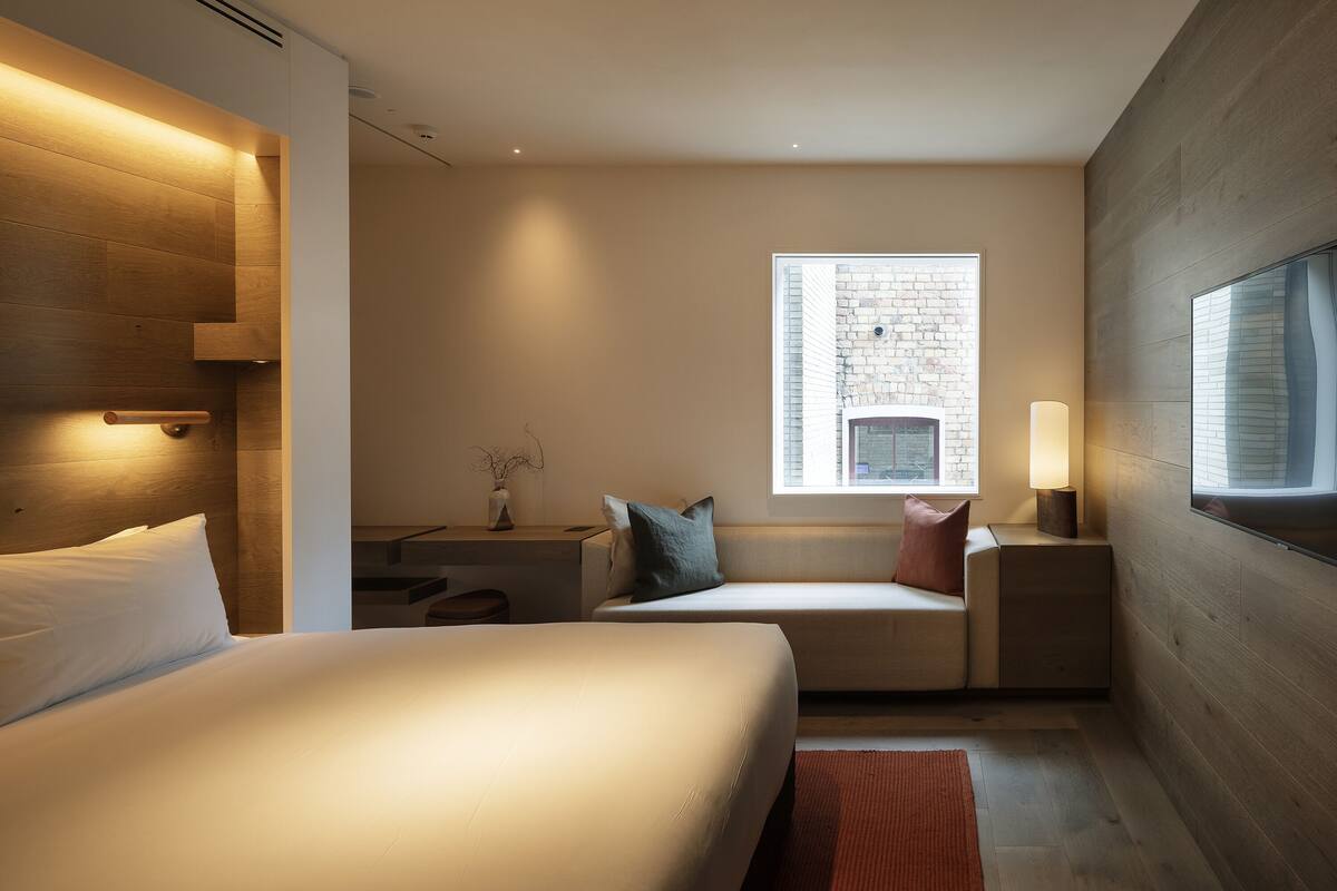 A modern hotel room with a large bed, a seating area with a view of the city, and a large window.