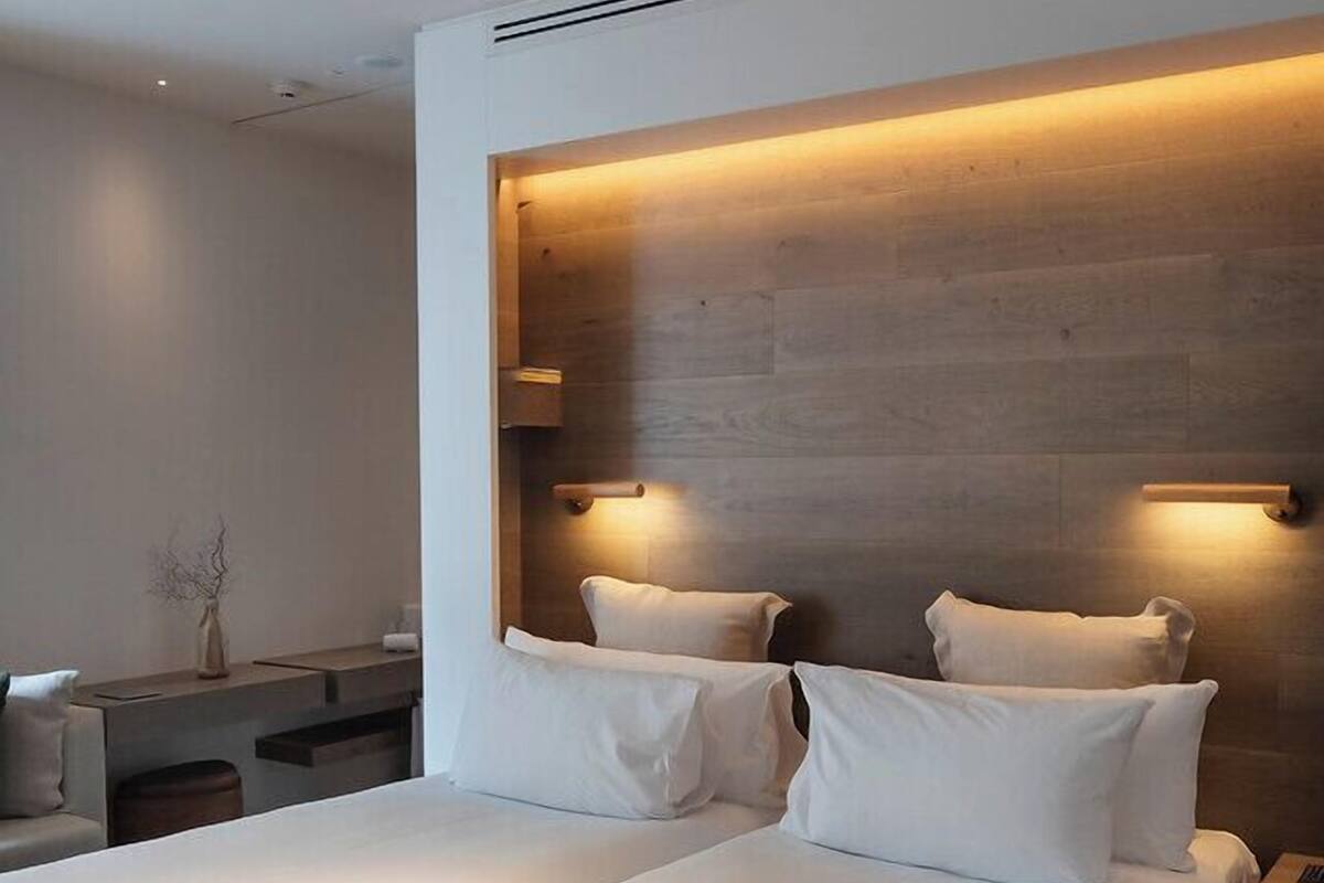 A modern hotel room with a large bed, bedside tables, and a wall-mounted light fixture.