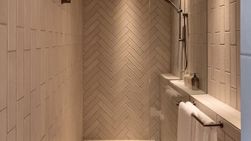 A modern bathroom with a herringbone-patterned wall, a shower with a handheld showerhead, and a towel rack with a white towel.