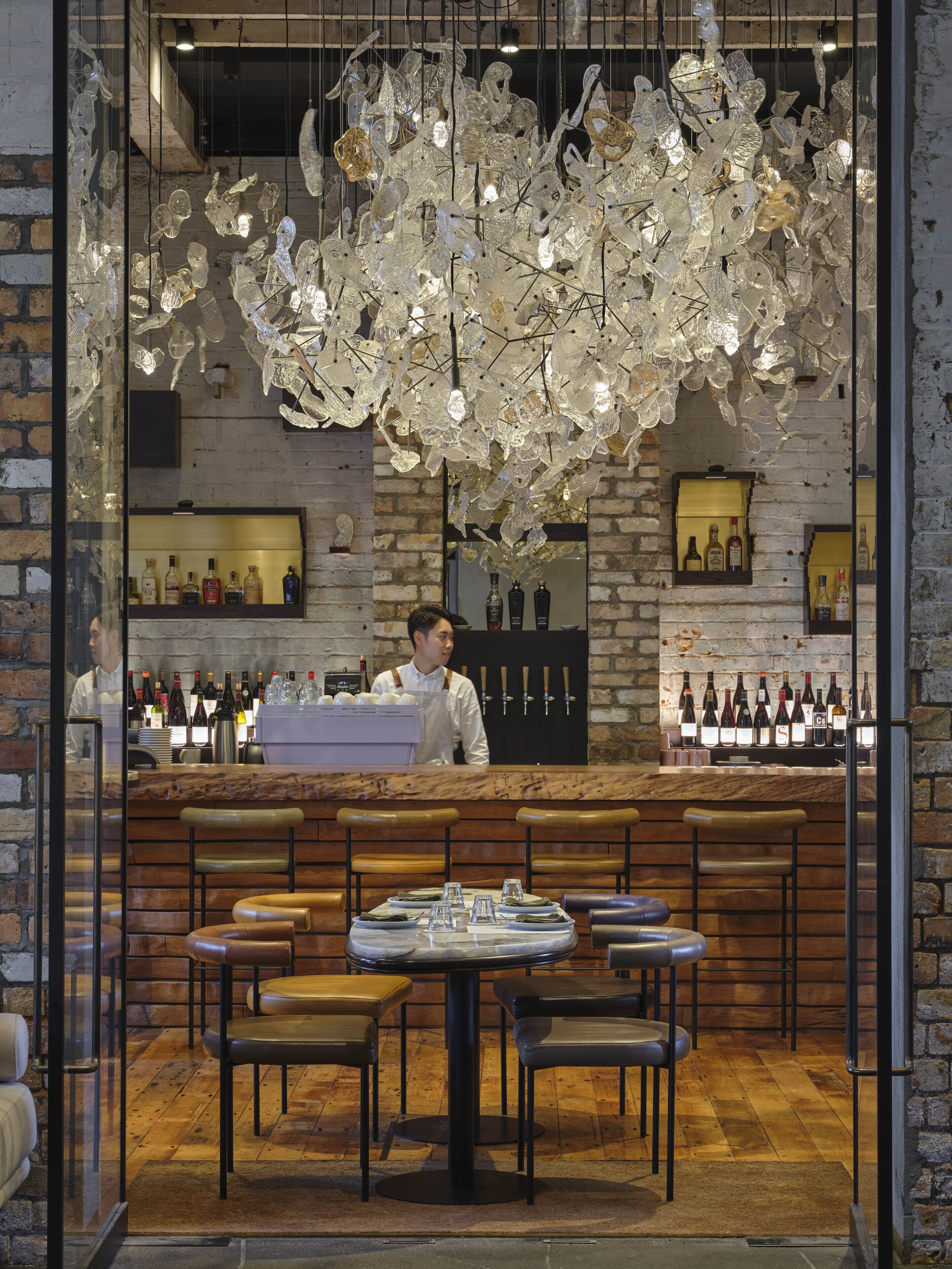 A restaurant interior with a bartender, wooden bar counter, and seating area.