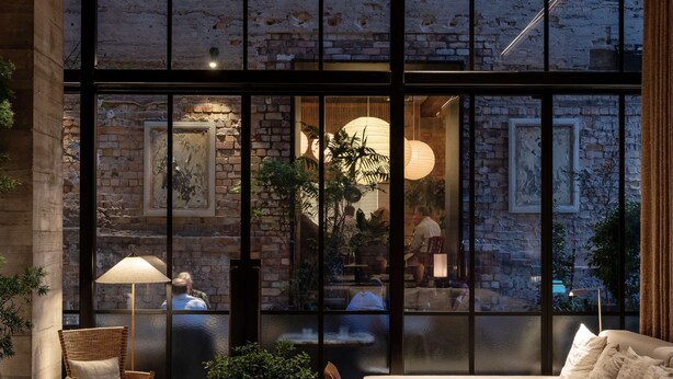 Un intérieur moderne avec des murs en briques, de grandes fenêtres et différents espaces de détente, notamment des canapés et des tables.