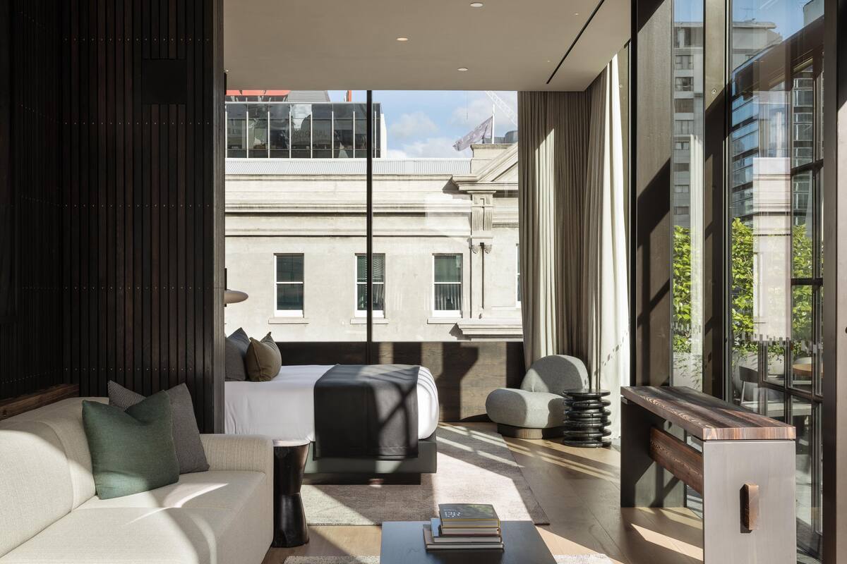 A modern living room with a sofa, a bed, a coffee table, and a view of a building through large windows.