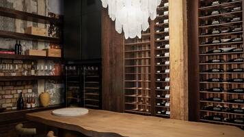 A bar area with a wooden bar counter, bar stools, a decorative chandelier, and wine racks.