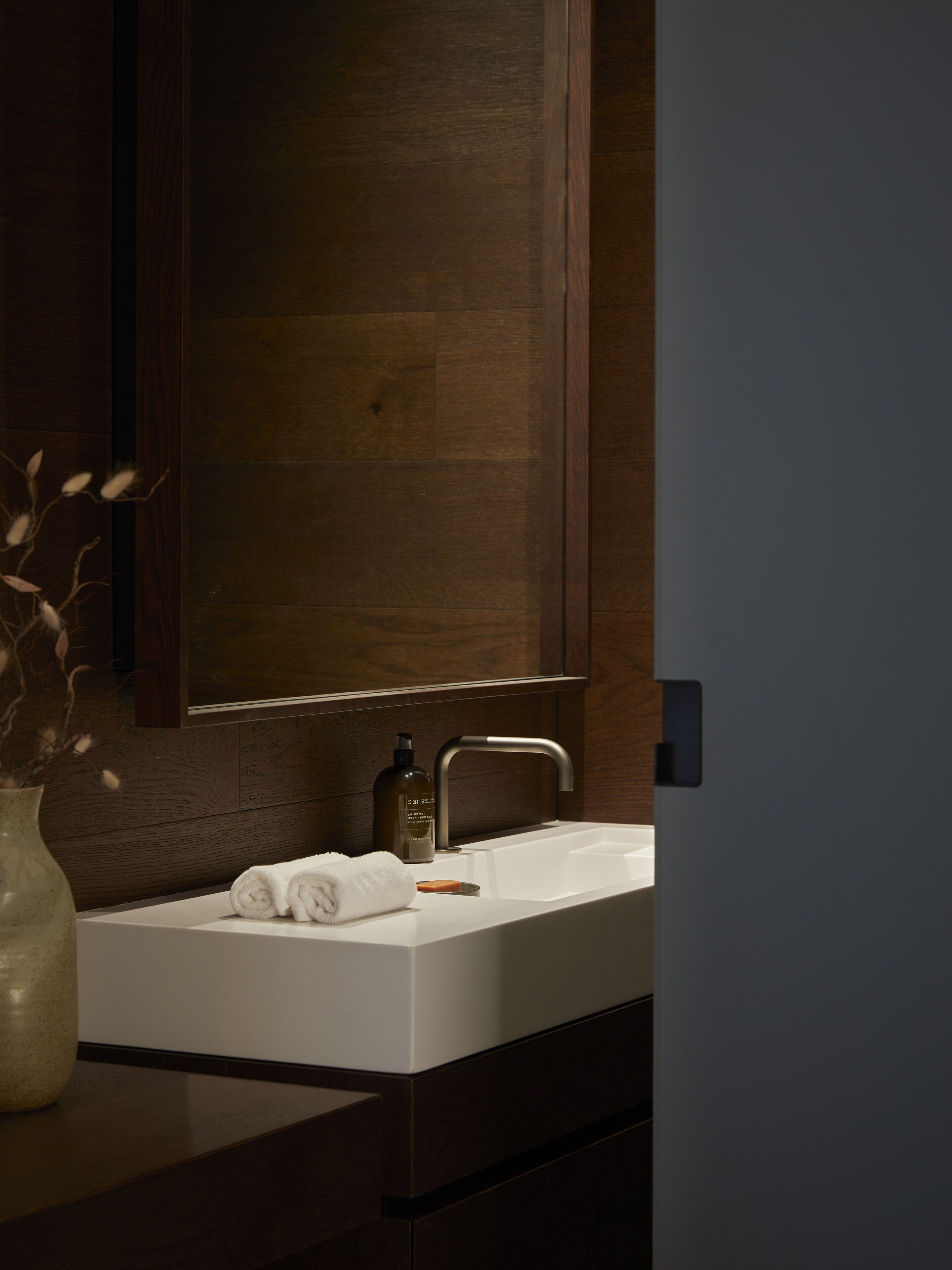 Un baño moderno con un lavabo blanco, muebles de madera oscura y un espejo grande.