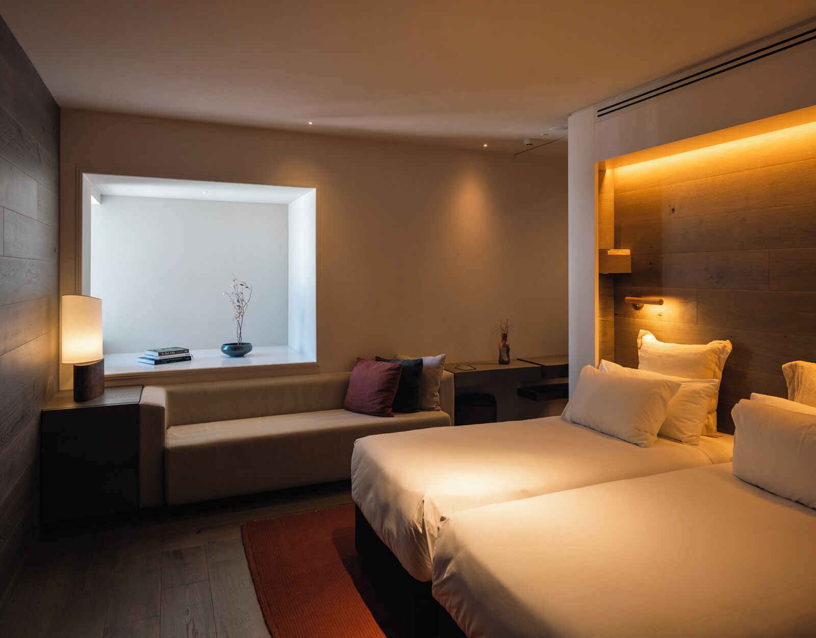 Een moderne hotelkamer met een groot raam, een bank, een bed en een nachtkastje met een lamp.