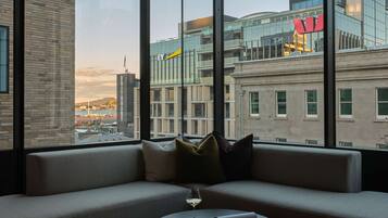 Ein modernes Hotelzimmer mit großem Fenster und Blick auf die Stadt, einer bequemen Couch, einem kleinen runden Tisch und einem Glas Wein.