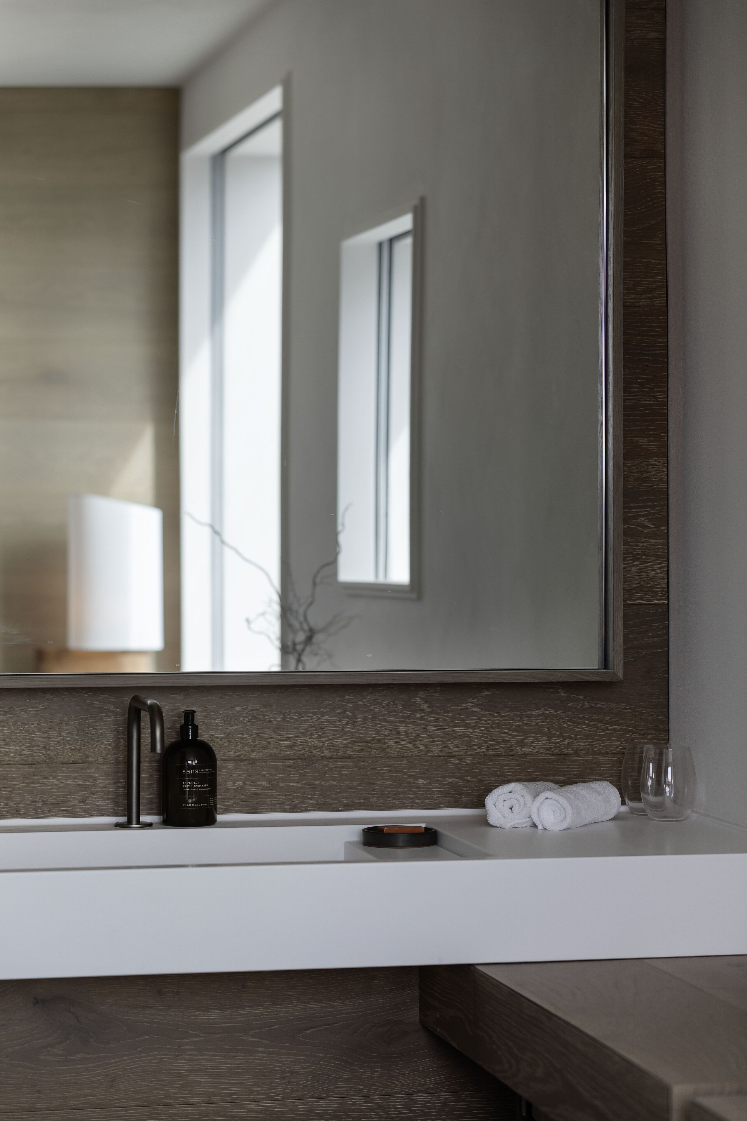 A modern bathroom with a large mirror, a white countertop, and a wooden vanity.