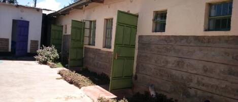 A building with multiple green doors and windows, a concrete pathway, and some vegetation.