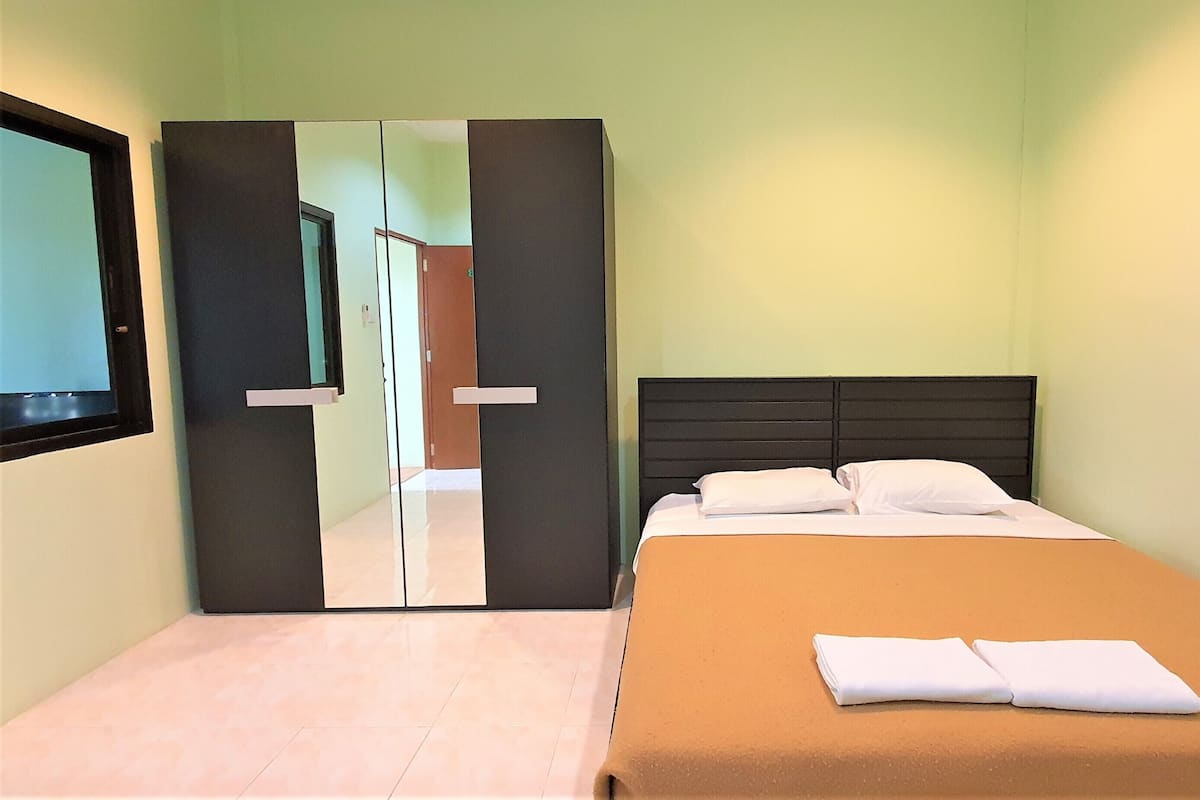 Une chambre d’hôtel avec un lit, une couverture marron, un oreiller blanc et un meuble-miroir.
