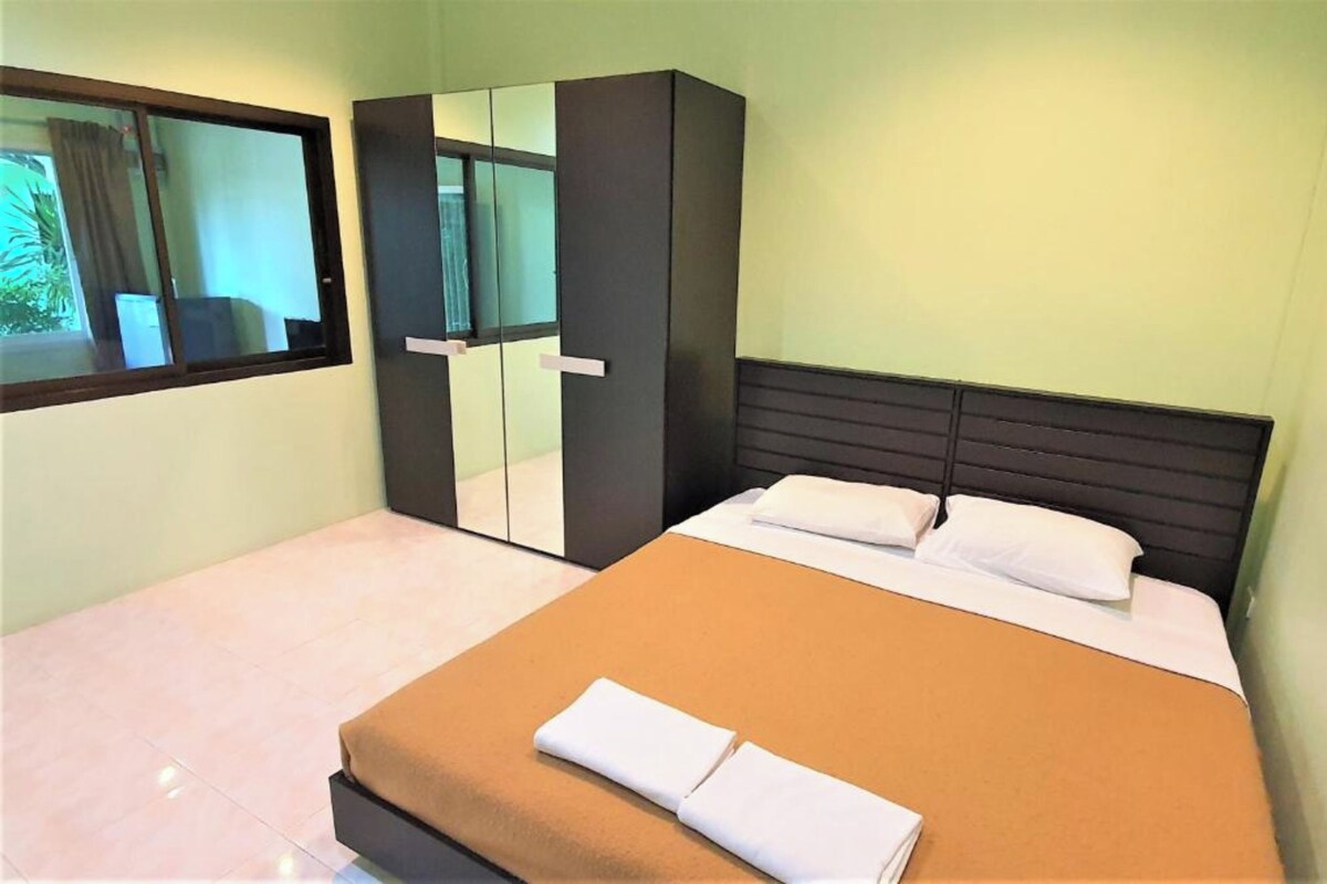 A hotel room with a bed, a wardrobe, a window, and a view of greenery outside.