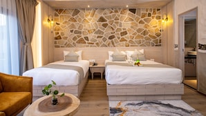 A hotel room with two beds, a wooden headboard, a stone wall, a small table with a plant, and a bathroom visible through an open door. - Arushi Boutique Hotel (Kathmandu)