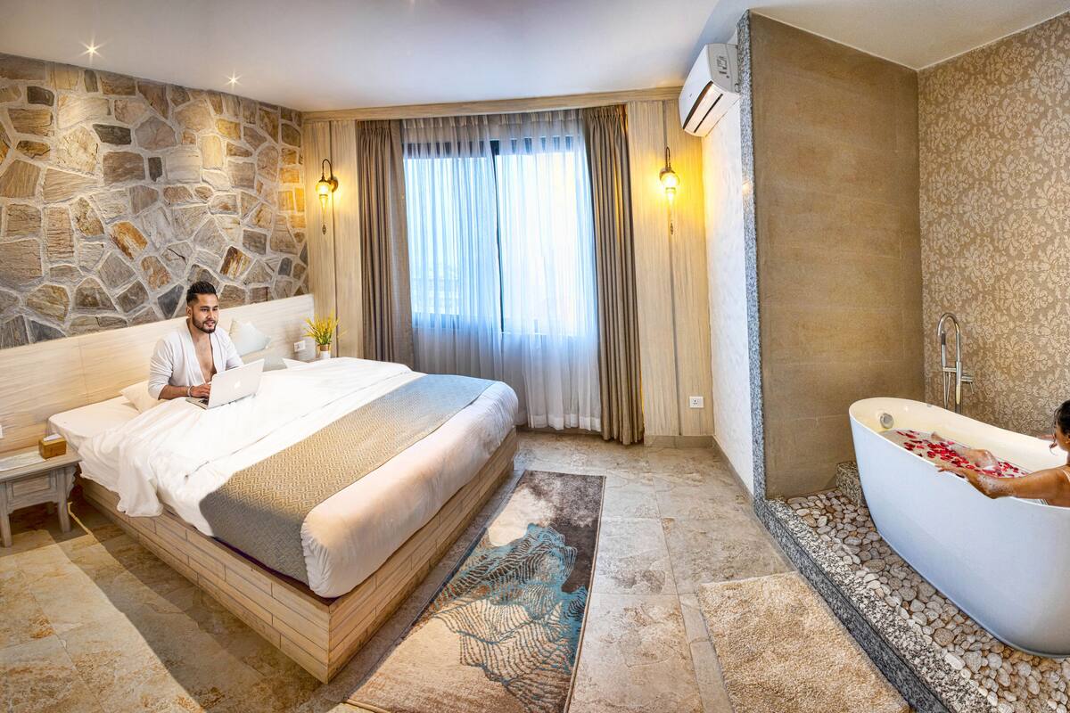 Een moderne hotelkamer met een stenen muur, een groot bed, een zithoek en een badkuip met rozenblaadjes.