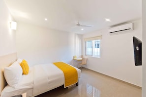 A hotel room with a bed, a desk, a chair, a window, and an air conditioning unit. - X by Bloom - Hebbal (Bengaluru)