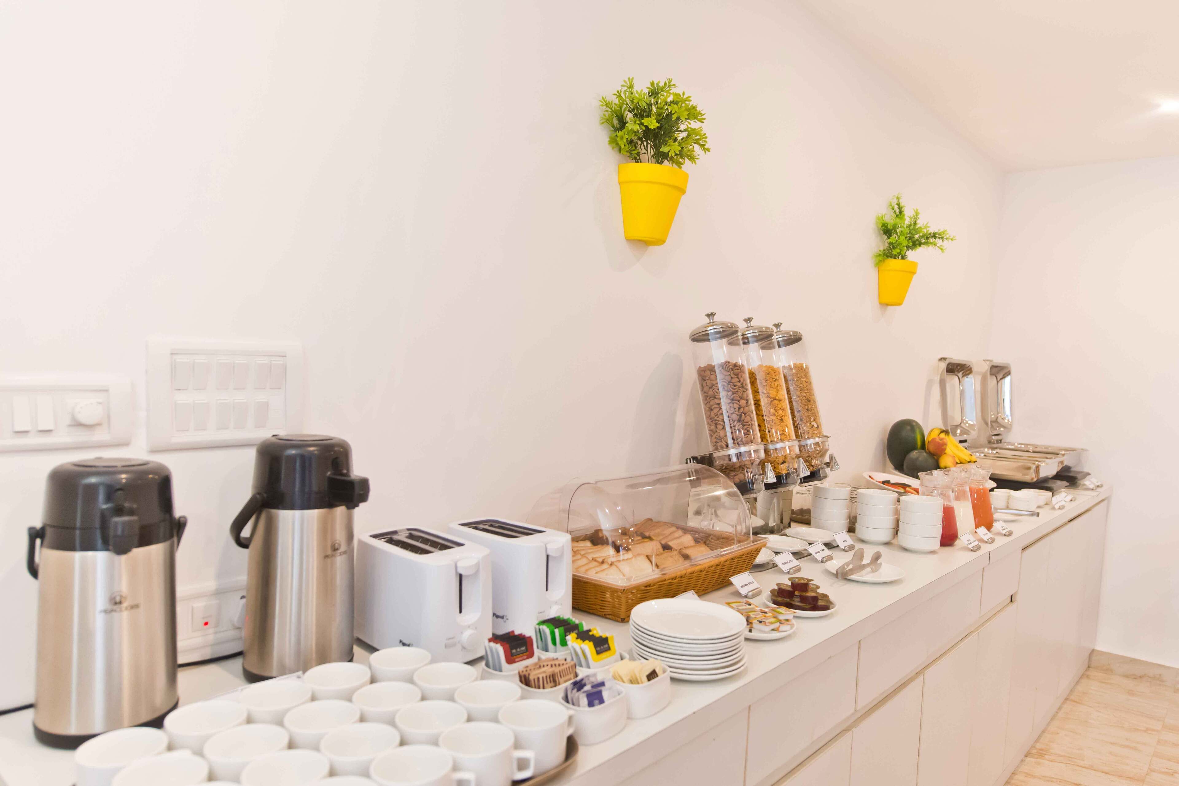 Montaje tipo bufé con diferentes alimentos, una estación de café y dos plantas en macetas en la pared.
