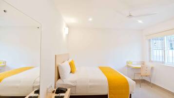 Una habitación de hotel con una cama grande, un escritorio, una silla y un ventilador de techo.