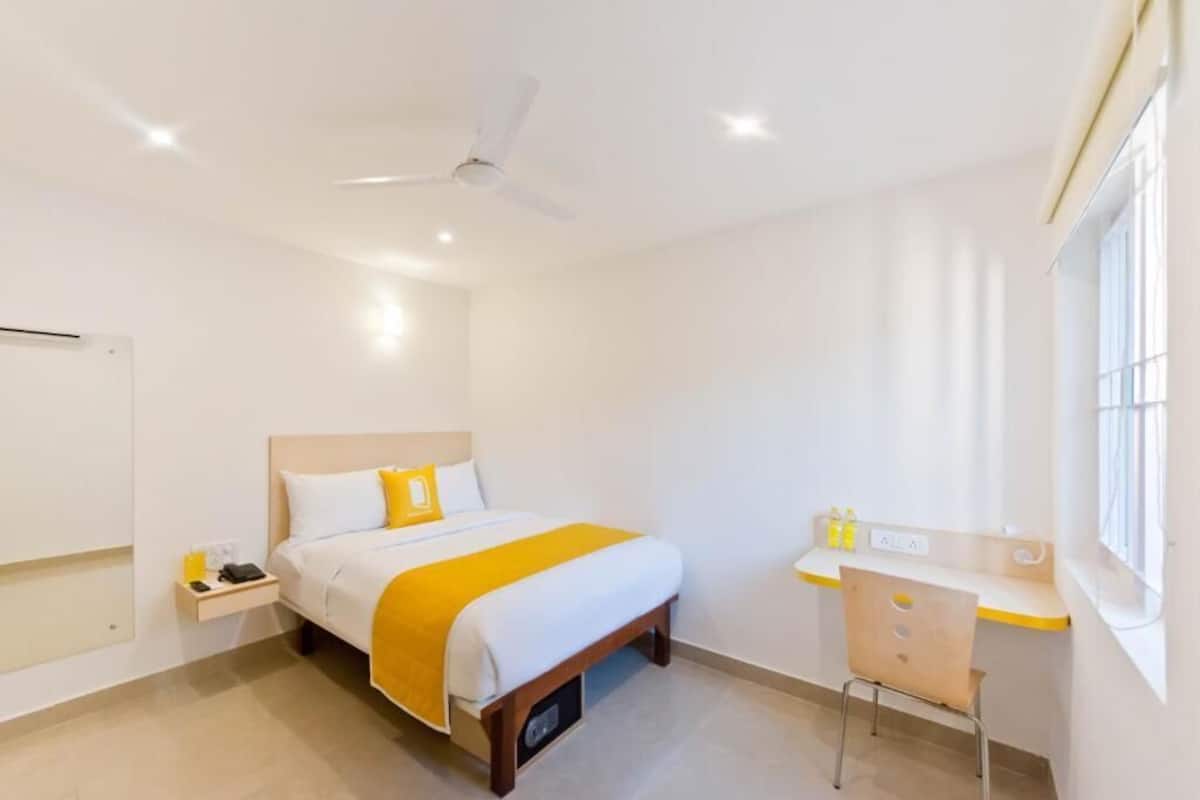 Una habitación de hotel con cama, mesita de noche, escritorio, silla y ventilador de techo.