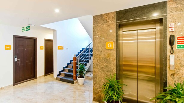 A hotel lobby with a marble floor, a staircase, an elevator, and a fire exit sign. - X by Bloom - Hebbal (Bengaluru)