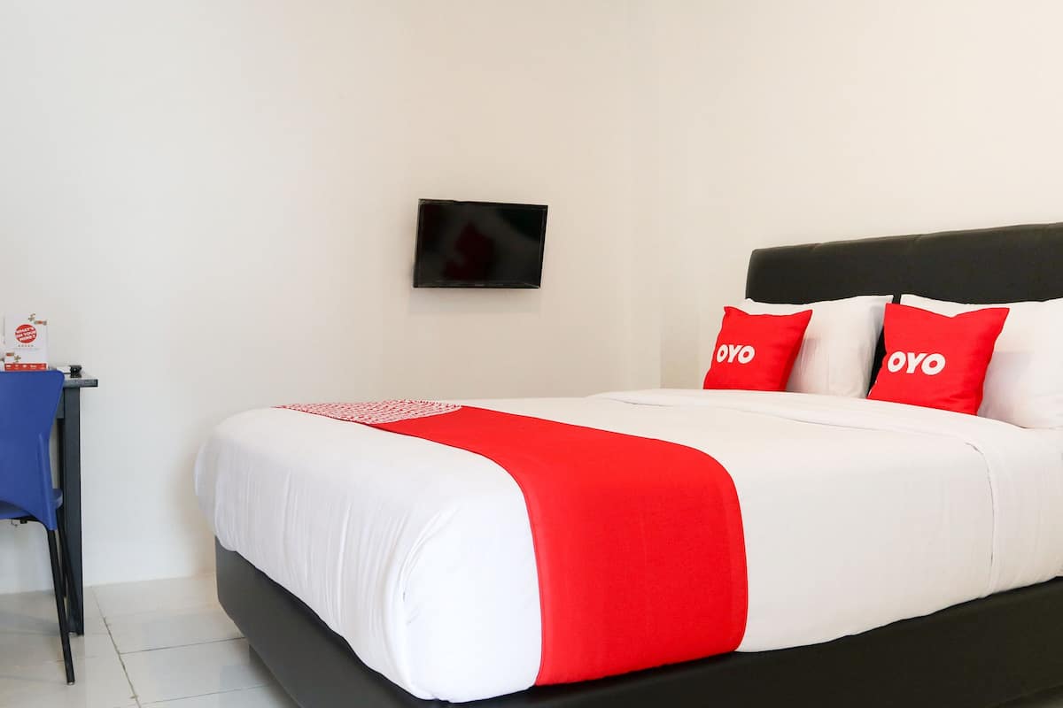 A neatly made bed with white and red bedding, a black headboard, and a small table with a blue chair beside it.