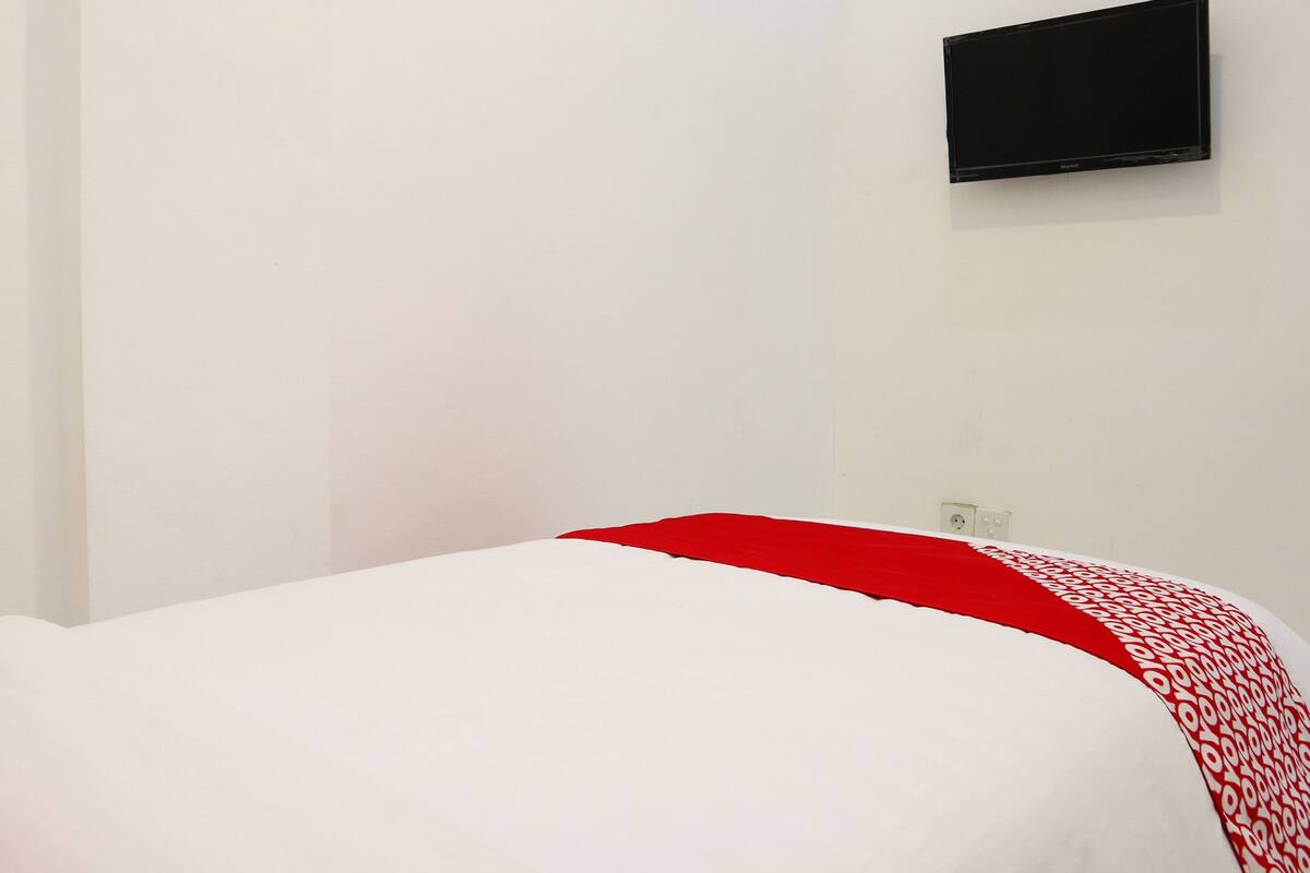 A room with a bed, a flat-screen TV mounted on the wall, and a power outlet.