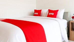 A bed with white and red bedding, two pillows with 'OYO' branding, and a wooden nightstand with a water bottle and flowers. - Hotel O Monalisa Residence And Cafe (Padang)