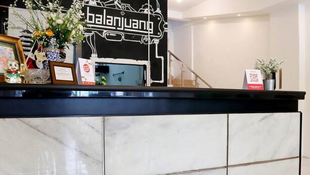 A reception desk with a marble design, a sign reading "balanjuang," and various items like a framed picture, a small figurine, and a vase with flowers. - Hotel O Monalisa Residence And Cafe (Padang)
